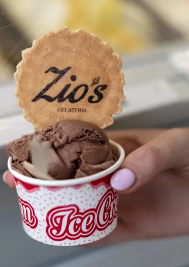 Llaw yn dal cwpan o gelato siocled gyda bisgedi wedi'i frandio yn Zio's Gelateria.