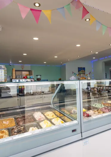 Tu mewn i Gelateria Zio gyda cownteri arddangos gwydr wedi'u llenwi â gelato a bunting lliwgar yn hongian o'r nenfwd.