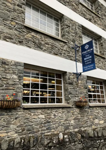 Golygfa allanol o adeilad melin wlân gerrig gyda ffenestri mawr.