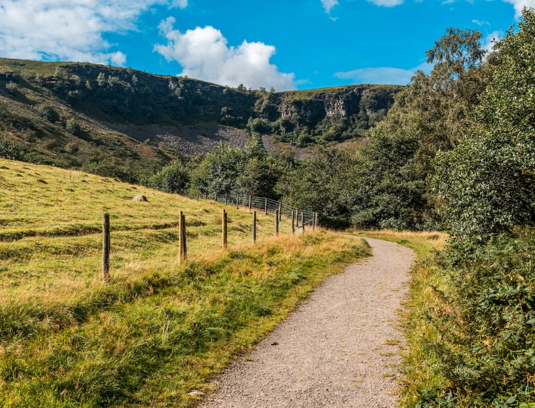 Llwybr cerdded o gwmpas cae gyda tharren werdd y tu cefn.