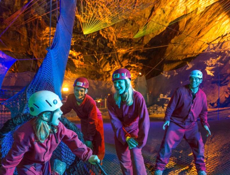 Grŵp o bobl ar rwydi’r parc trampolîn tanddaearol Bounce Below yn Zip World Slate Caverns.