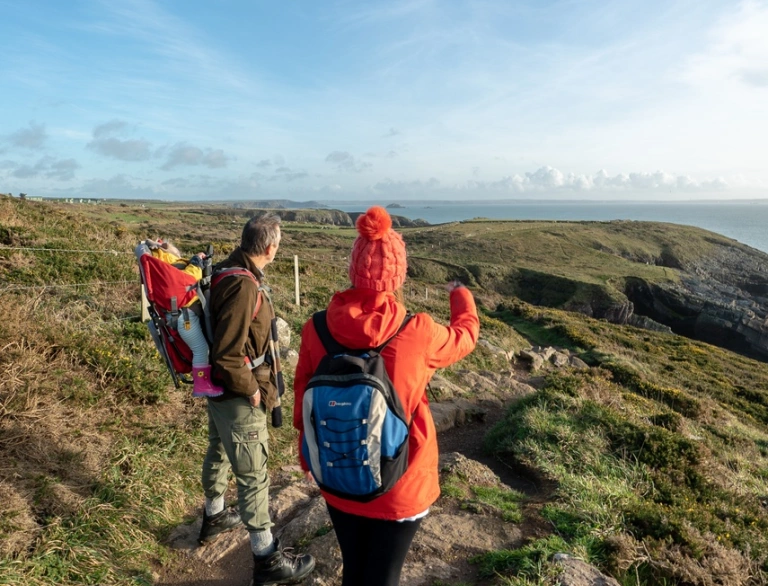 Teulu ifanc â babi mewn cludwr cefn ar Lwybr Arfordir Cymru