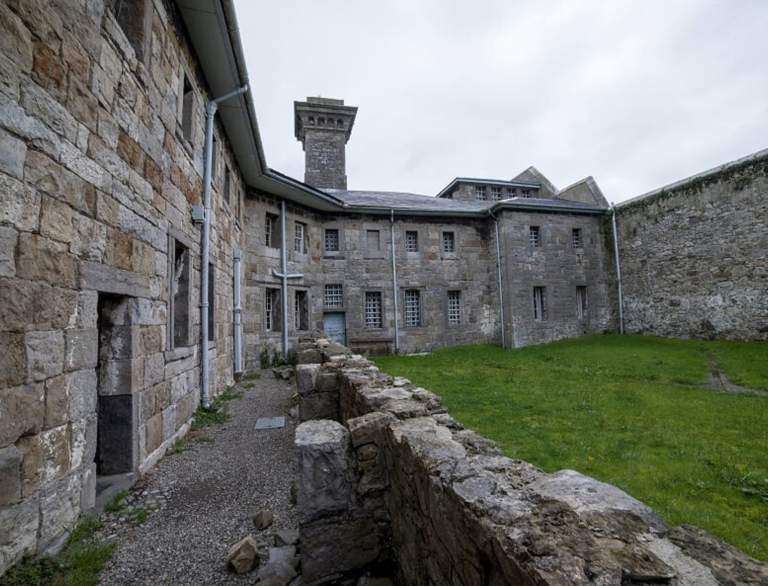 Yr iard mewn carchar cerrig – ardal laswelltog gyda chelloedd o’i chwmpas.