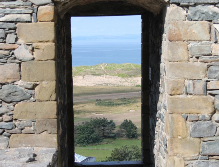 Golygfeydd drwy ddrws castell tuag at draeth.