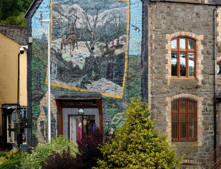 Tŷ gyda murlun wedi’i baentio ar ei ochr.