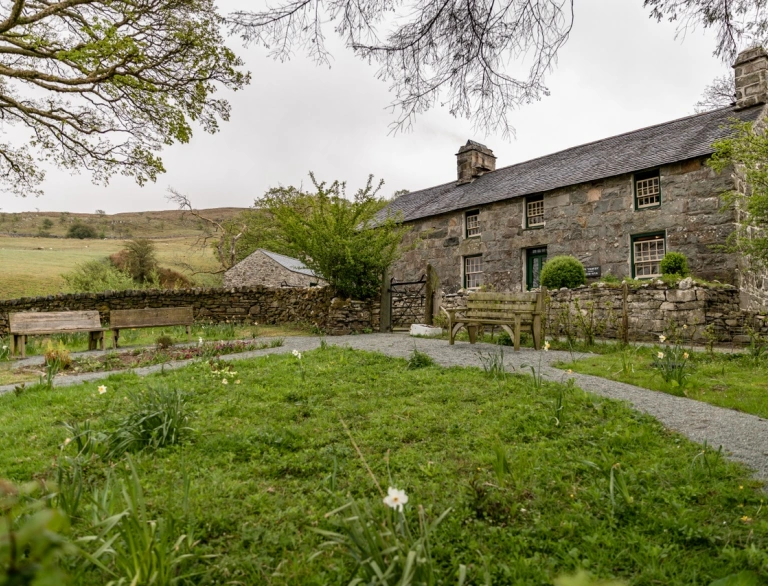 Tu allan i hen ffermdy carreg a gardd o'i flaen.