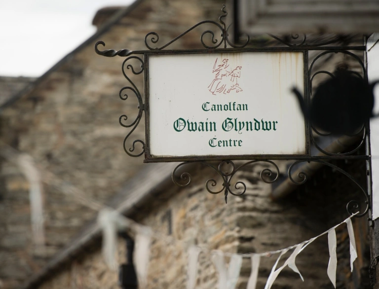 Arwydd tu allan i adeilad hynafol cerrig yn dweud 'Canolfan Owain Glyndŵr Centre'.
