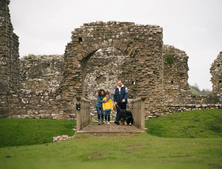 Teulu a chi yn archwilio adfeilion castell.