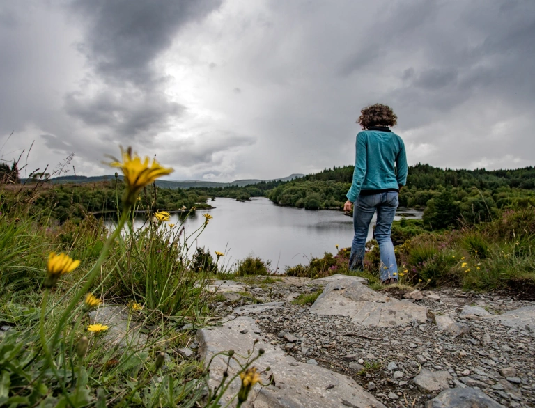 A woman walking a footpath towards a lake. The lake is surrounded by woodland.
