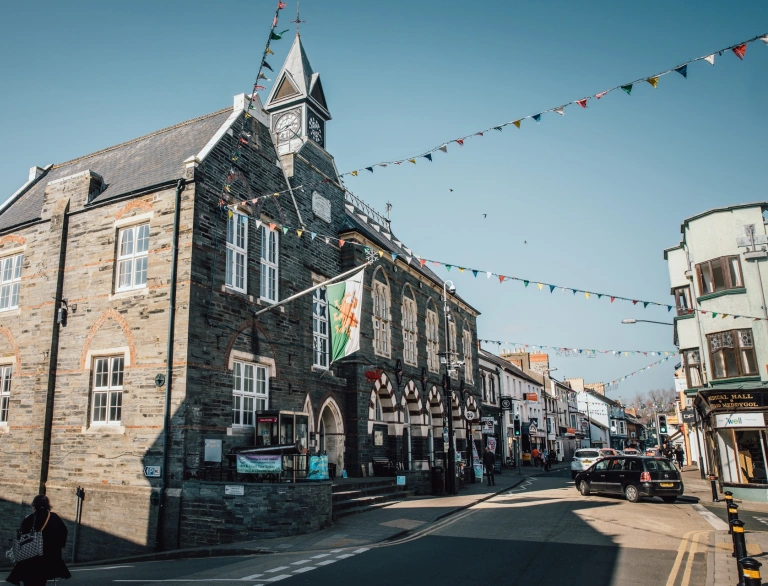 Canol tref Aberteifi. Adeilad cerrig gyda fflag y ddraig goch arni.