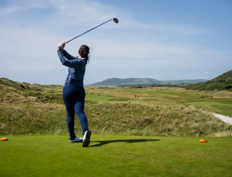 Golffwraig yn swingio clwb ar gwrs golff.