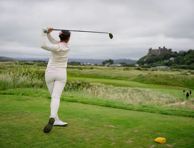 Golffwraig yn swingio clwb ar gwrs golff gyda chastell yn y cefndir.