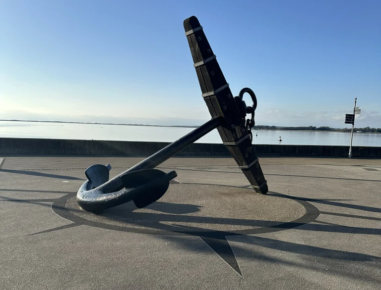 Large maritime anchor sculpture on Caernarfon waterfront overlooking the Menai Strait under a clear blue sky