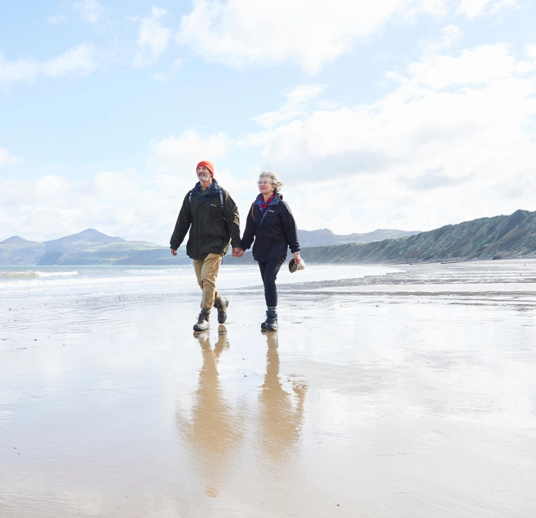 Cwpwl yn cerdded ar draeth Porthdinllaen