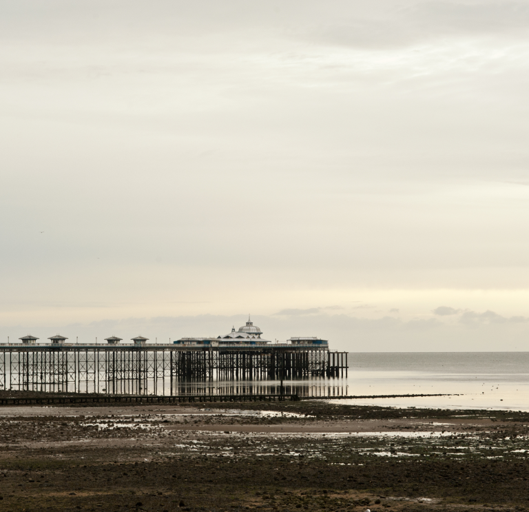 Pier Llandudno yn y pellter o'r lan