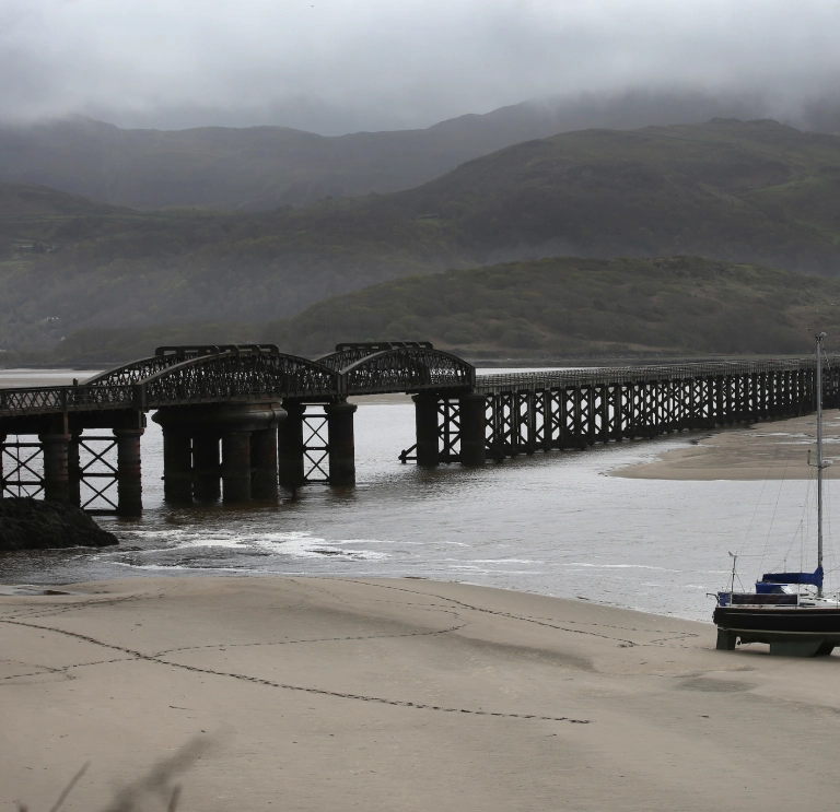 Pont rheilffordd a chwch bychan adeg llanw isel