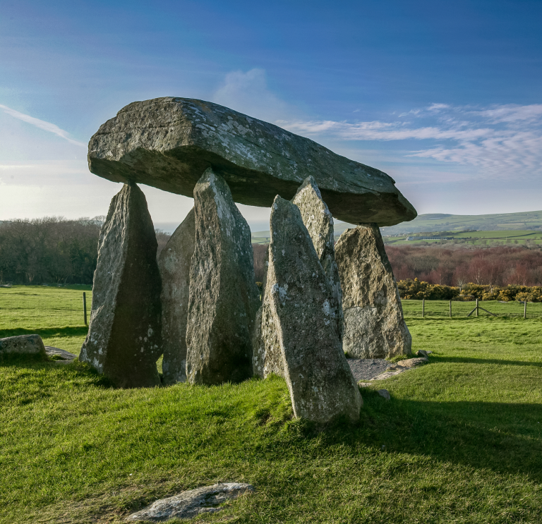 Llun o gerrig y siambr gladdu mewn cae gyda bryniau yn y pellter