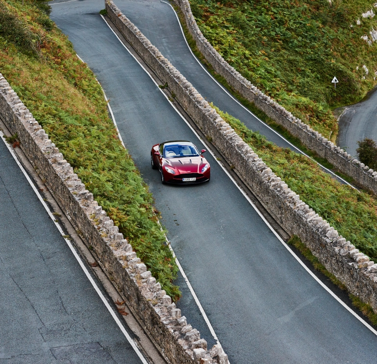 Llun o'r awyr o gar Aston Martin coch yn gyrru ar hyd ffordd