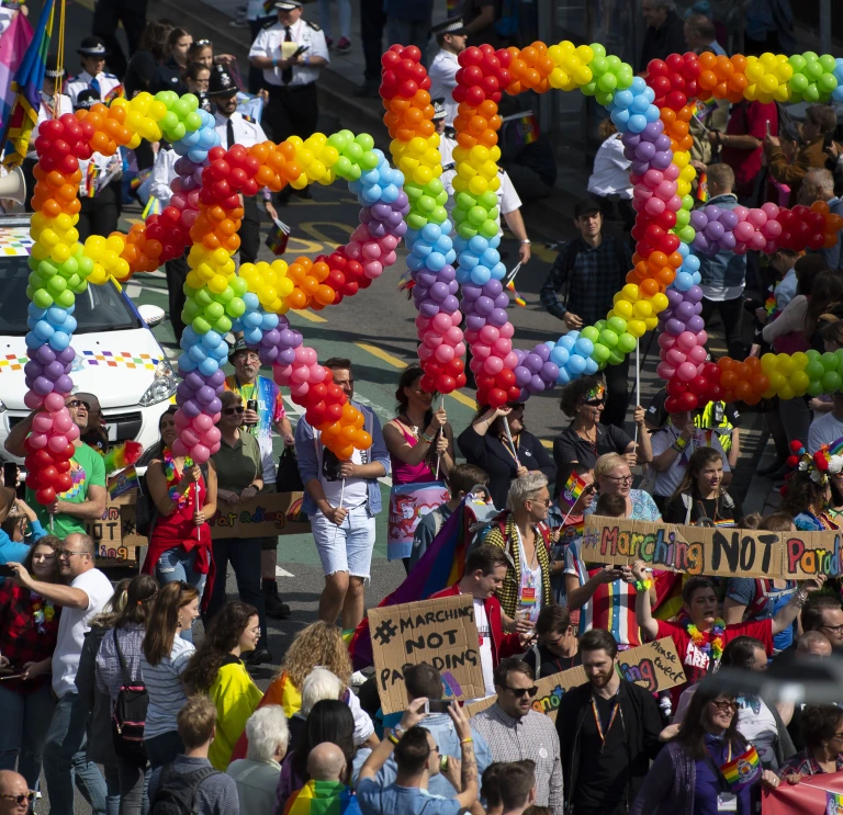 Torf o bobl yn gafael mewn balŵns sy’n dweud Pride.