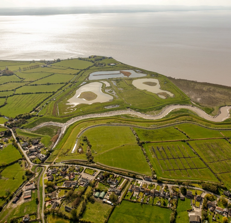 Golygfa o’r awyr o dirwedd werdd a dyfrffyrdd ger afon.