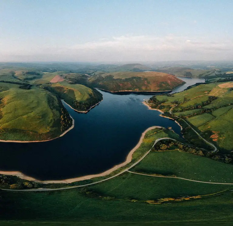 panorama o gronfa wydr a bryniau gwyrdd gyda'r haul