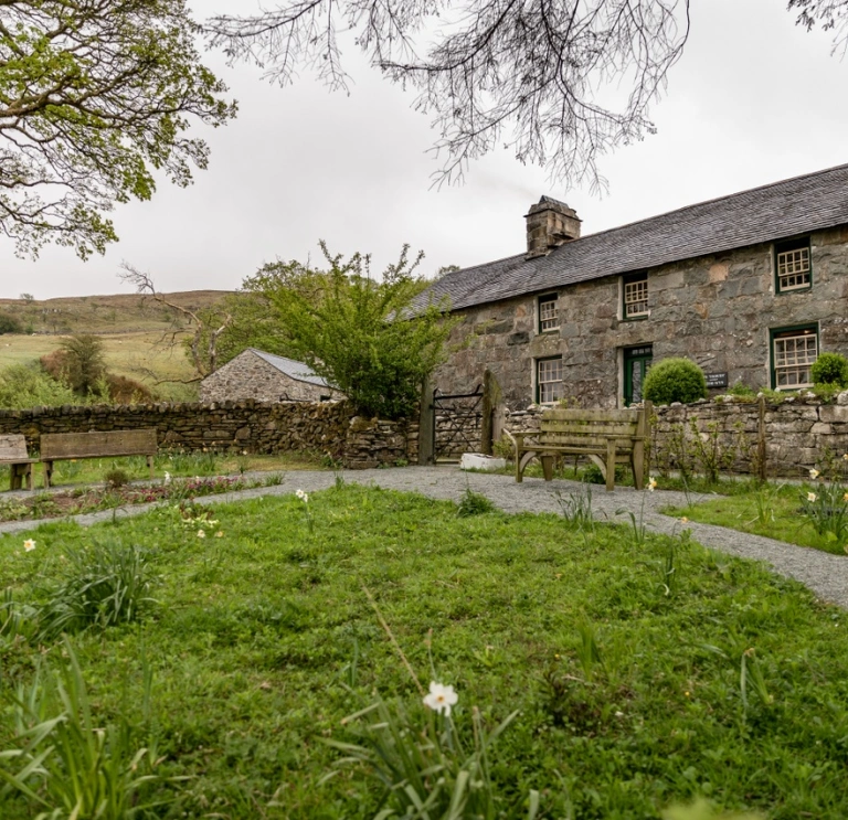 Tu allan i hen ffermdy carreg a gardd o'i flaen. 