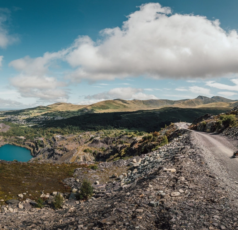 Quarry Kart yn Zip World yn erbyn cefndir o fynyddoedd a phwll glas.