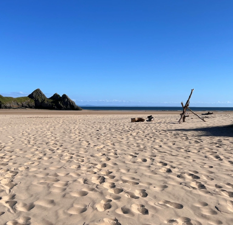 Traeth llydan, tywodlyd gyda chlogwyni wedi'u jagged un ochr a thwyni tywod y llall.