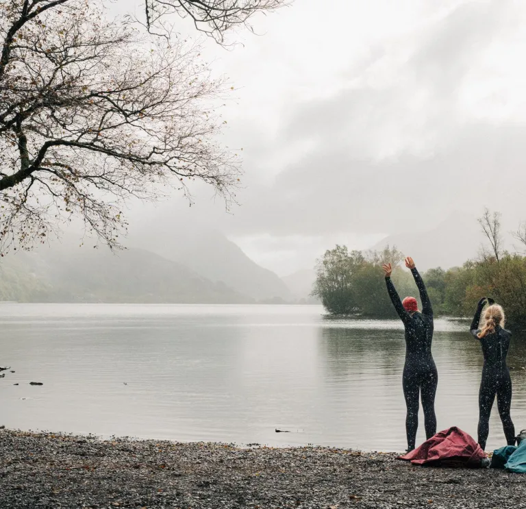 Tri ffrind yn nofio mewn dŵr oer yn Llyn Padarn, Parc Cenedlaethol Eryri (Eryri), Gogledd Cymru