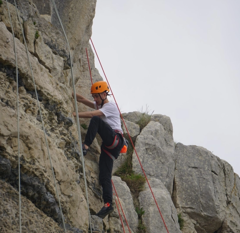 dyn yn gwisgo offer diogelwch wrth ddringo wyneb craig.