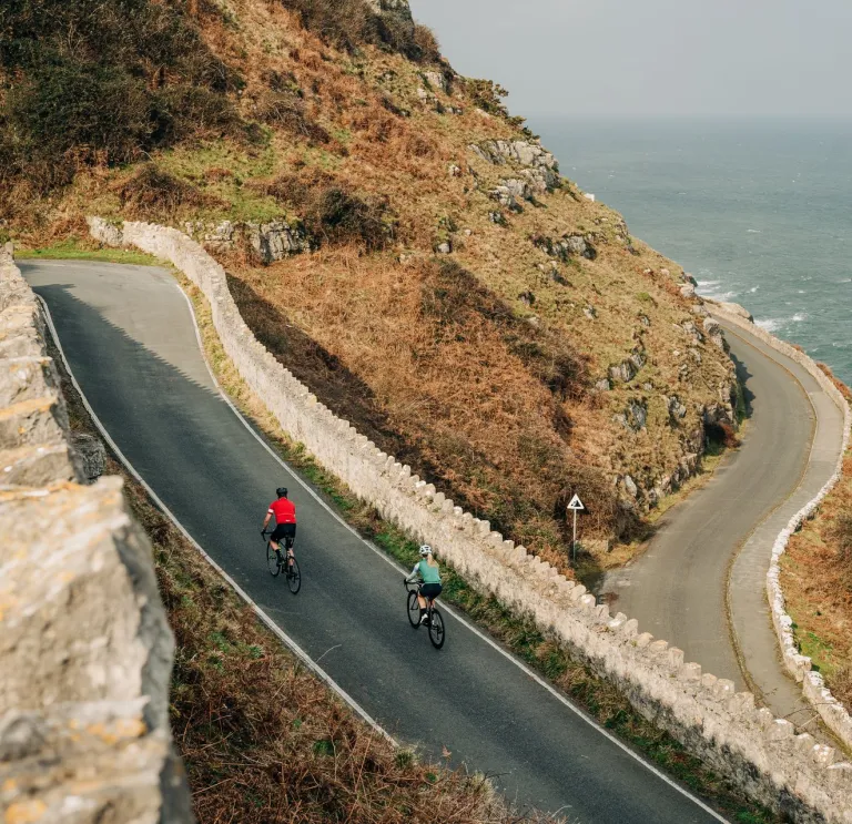 Llun o'r awyr o ffordd gefn gyda 2 feiciwr yn dringo'r rhan fwy serth yn y blaendir.