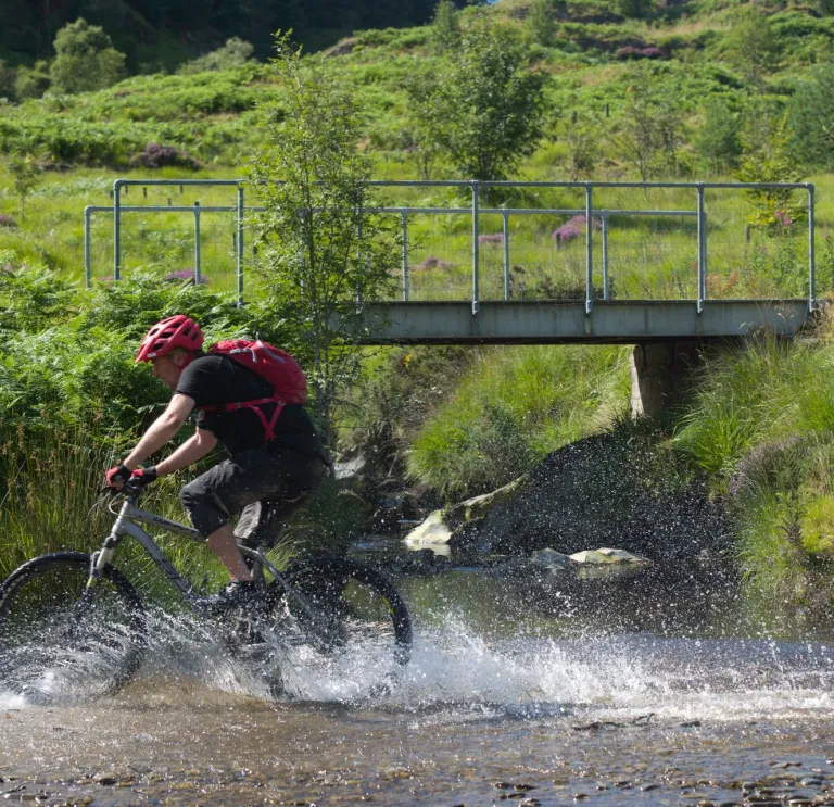 Beiciwr yn torri trwy afon yng Ngheredigion