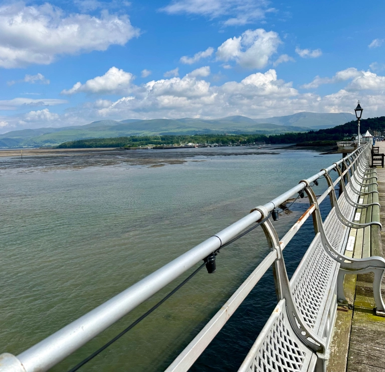 Edrych i lawr pier hir arddull Fictoraidd gyda'r pentir a'r môr yn y pellter.