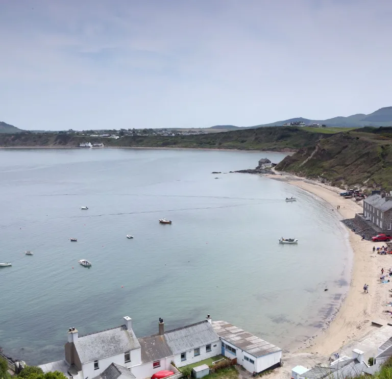 High up view over a curved sandy beach with clear blue waters, with buildings along the cliff edge.