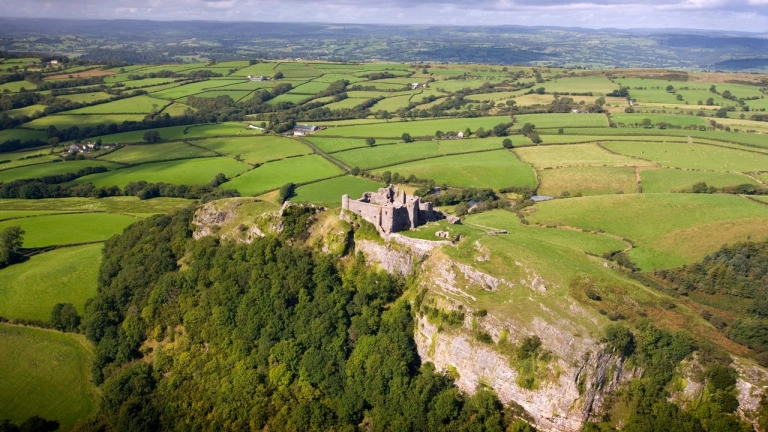 Golygfa o’r awyr o gastell ar fryn yng nghanol caeau gwyrdd.