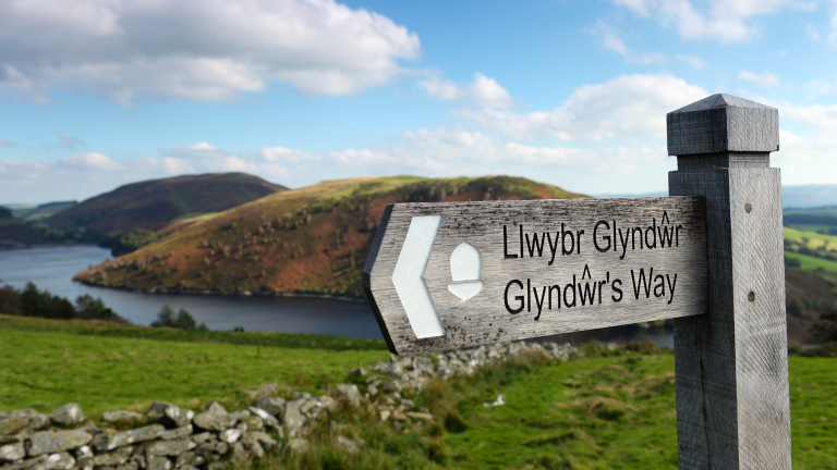 Arwydd Llwybr Glyndŵr gyda Llyn Clywedog a bryniau yn y cefndir
