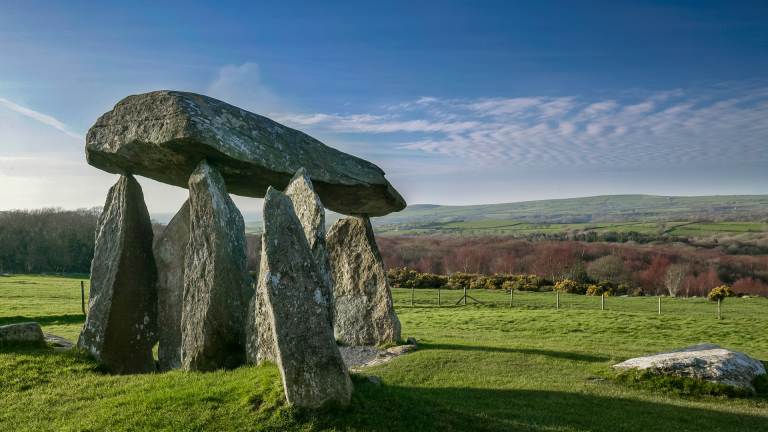 Llun o gerrig y siambr gladdu mewn cae gyda bryniau yn y pellter