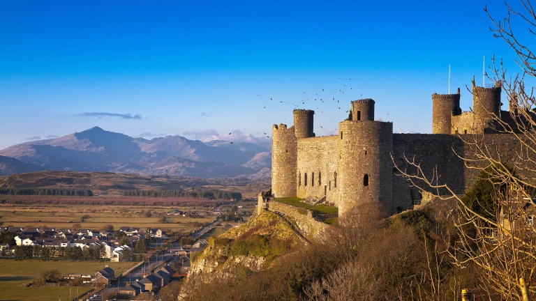 Castell ar fryn wedi’i amgylchynu gan gefn gwlad gyda mynyddoedd yn y cefndir