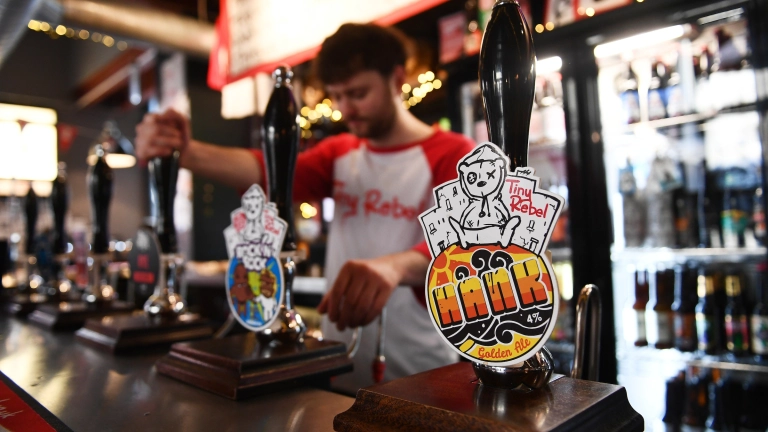 Barman yn tynnu peint a tapiau cwrw lliwgar ar y bar pren.
