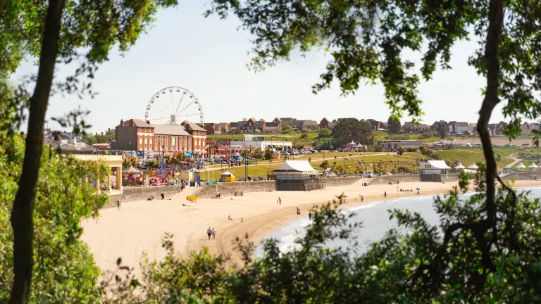 Edrych ar draeth a’r ffair drwy’r coed.