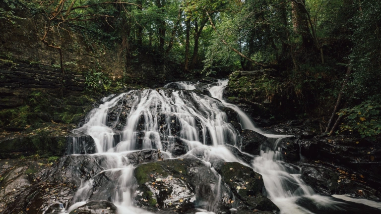 Rhaeadr yn llif llawn, gyda choed o amgylch.