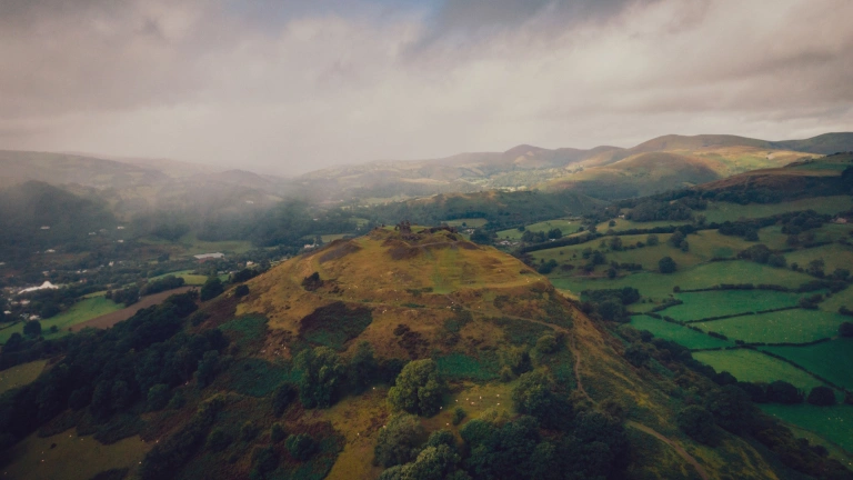 Llun o'r awyr o gastell ar fryn yng nghanol caeau gwyrdd. Mae'r awyr yn llwyd a chymylog.
