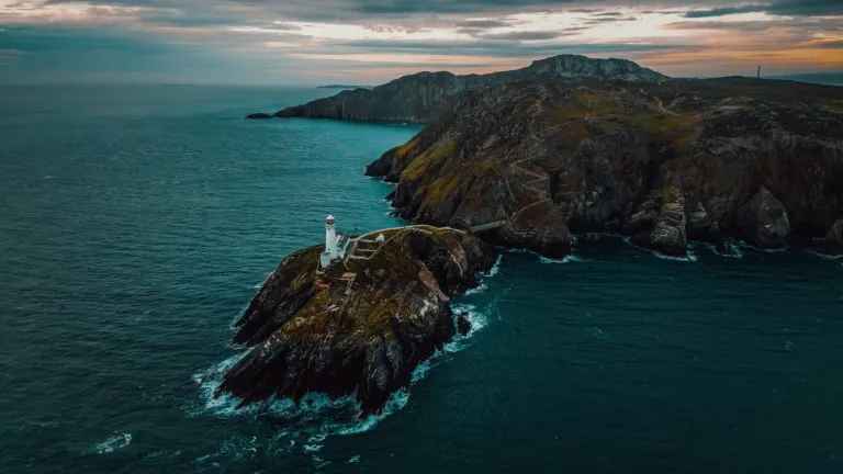 Goleudy ar benrhyn creigiog yn erbyn môr ac awyr las tywyll