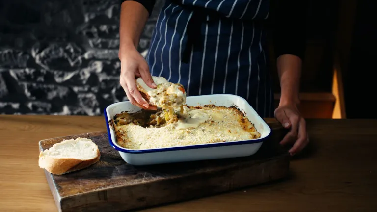 Tegell rostio gyda wyau Môn wedi'u pobi'n ffres, gyda llaw cogydd yn llwytho rhai ar sleisen o frechdan wedi ei dorri