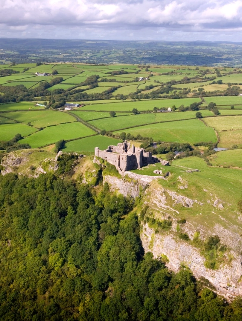 Golygfa o’r awyr o gastell ar fryn yng nghanol caeau gwyrdd.