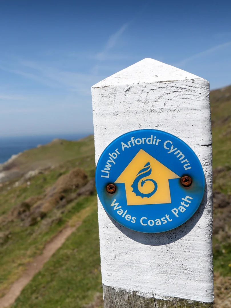 Arwyddbost ar lwybr yr arfordir yn edrych dros ddŵr.