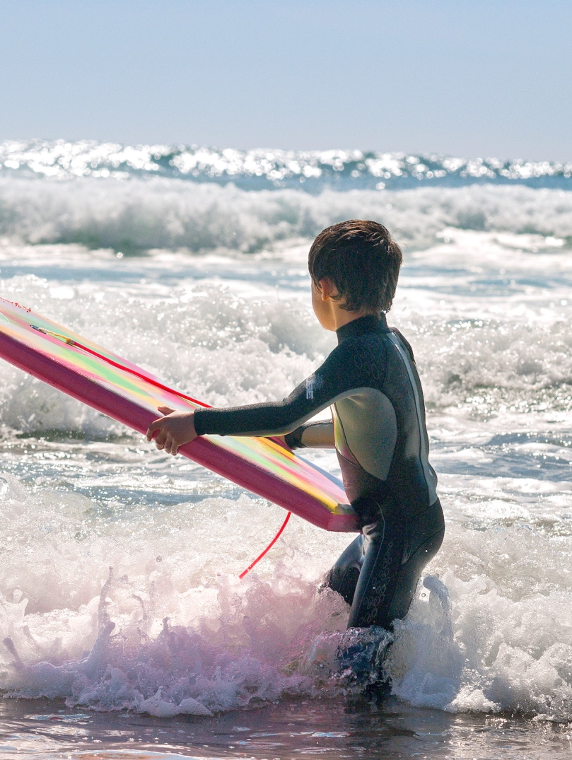 Plentyn yn sefyll yn y môr yn dal bodyboard
