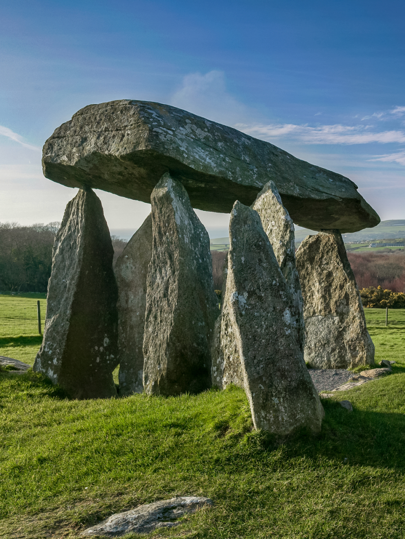 Llun o gerrig y siambr gladdu mewn cae gyda bryniau yn y pellter