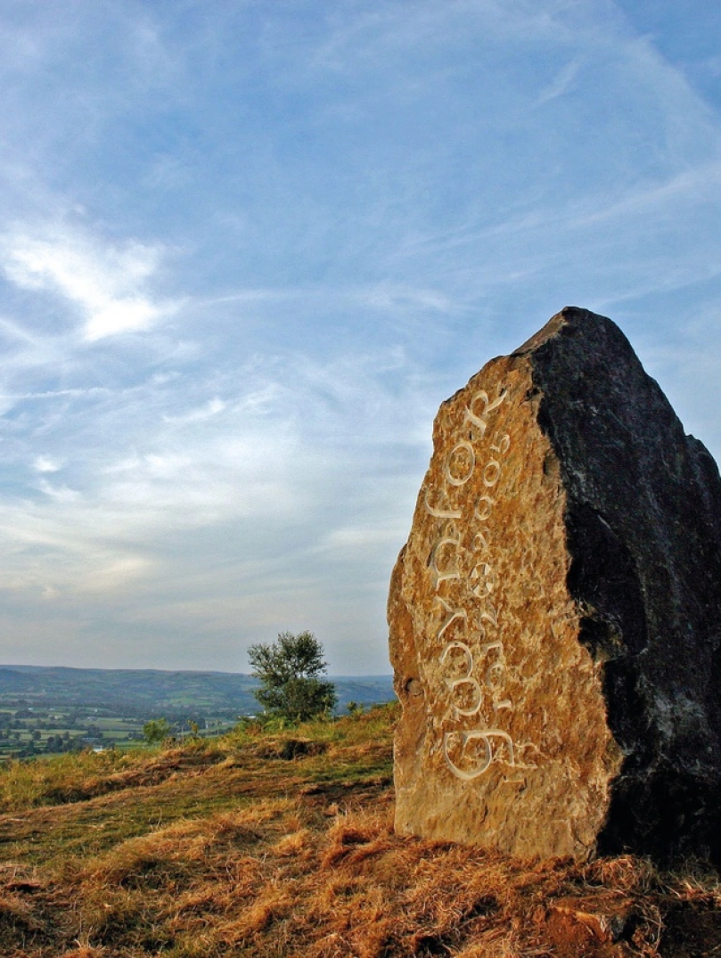 Craig fawr gyda mynyddoedd yn y cefndir ac awyr las