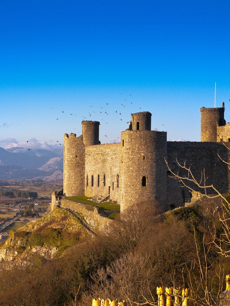 Castell ar fryn wedi’i amgylchynu gan gefn gwlad gyda mynyddoedd yn y cefndir